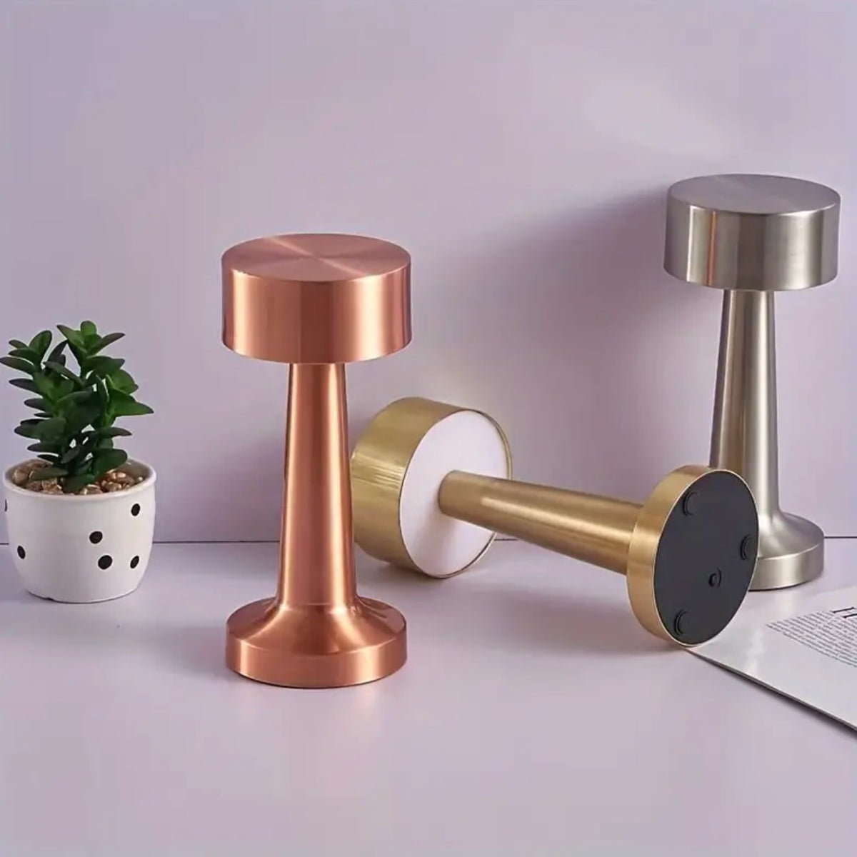 Venla table lamp in rose gold standing beside a gold one lying on its side