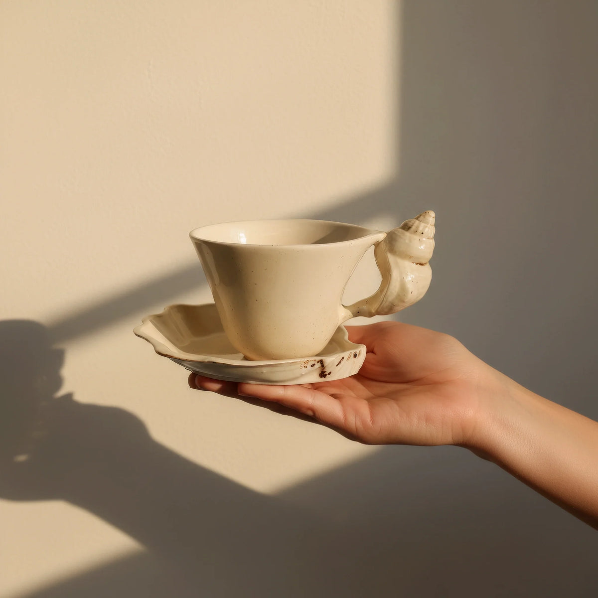 Hand holding the cup and shell saucer in warm window light