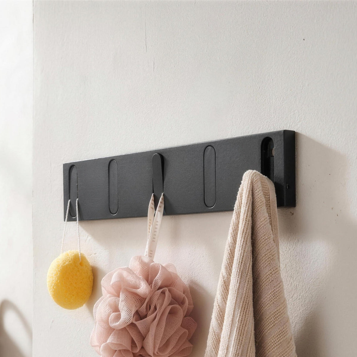 Black wall hook rack with five flip out hooks holding a towel and bath sponges