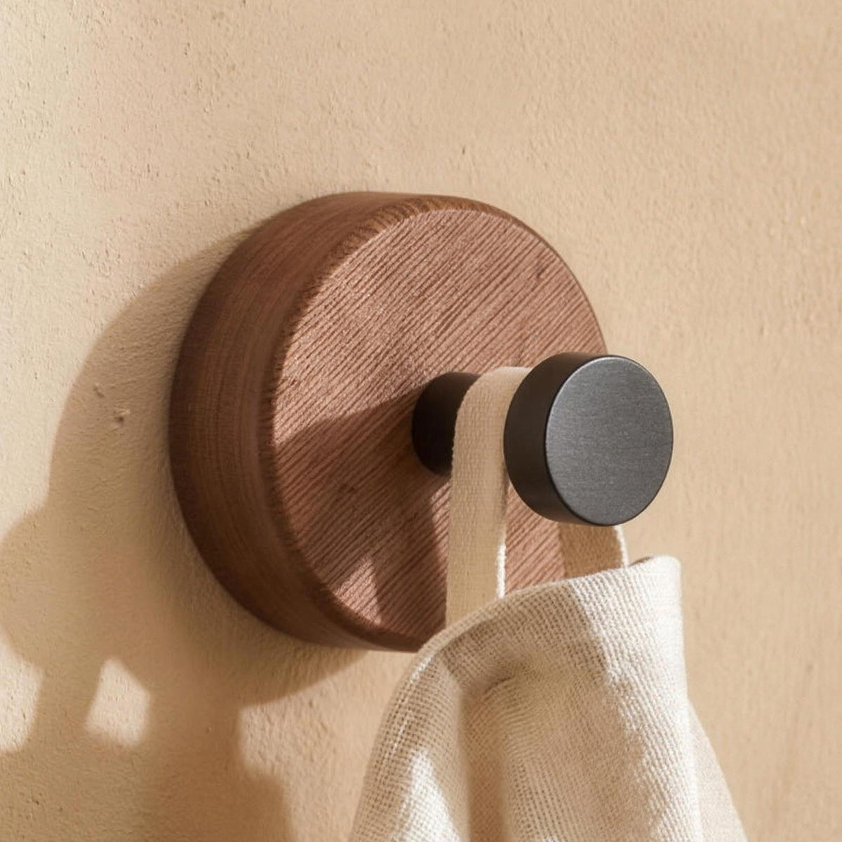 Round walnut wall hook with a matte black peg on a wall