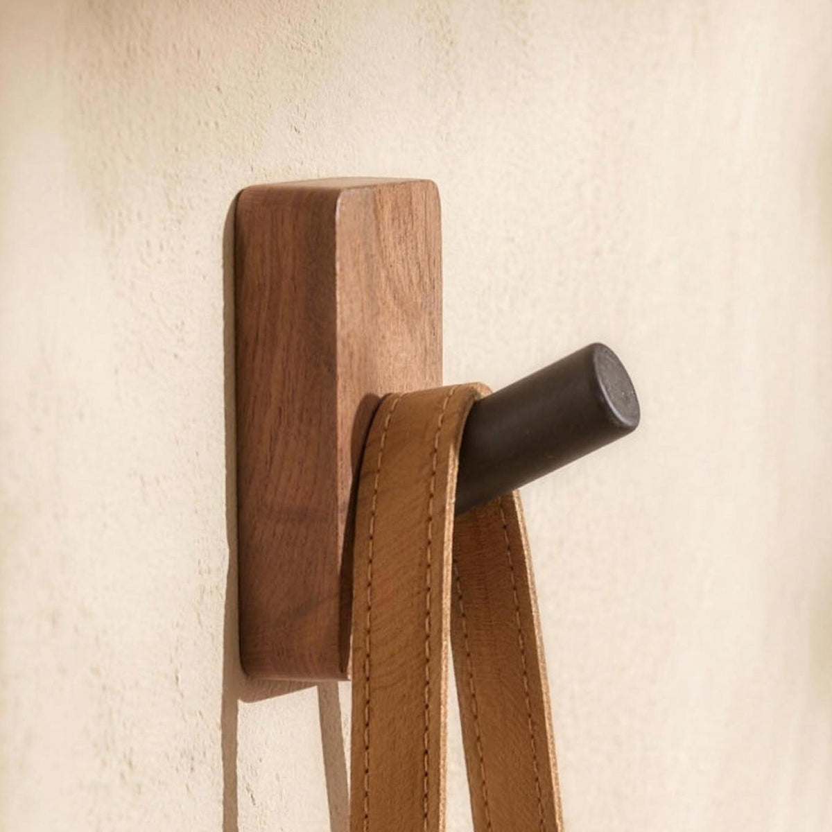 Walnut wall hook in Peg with a leather strap on a plaster wall