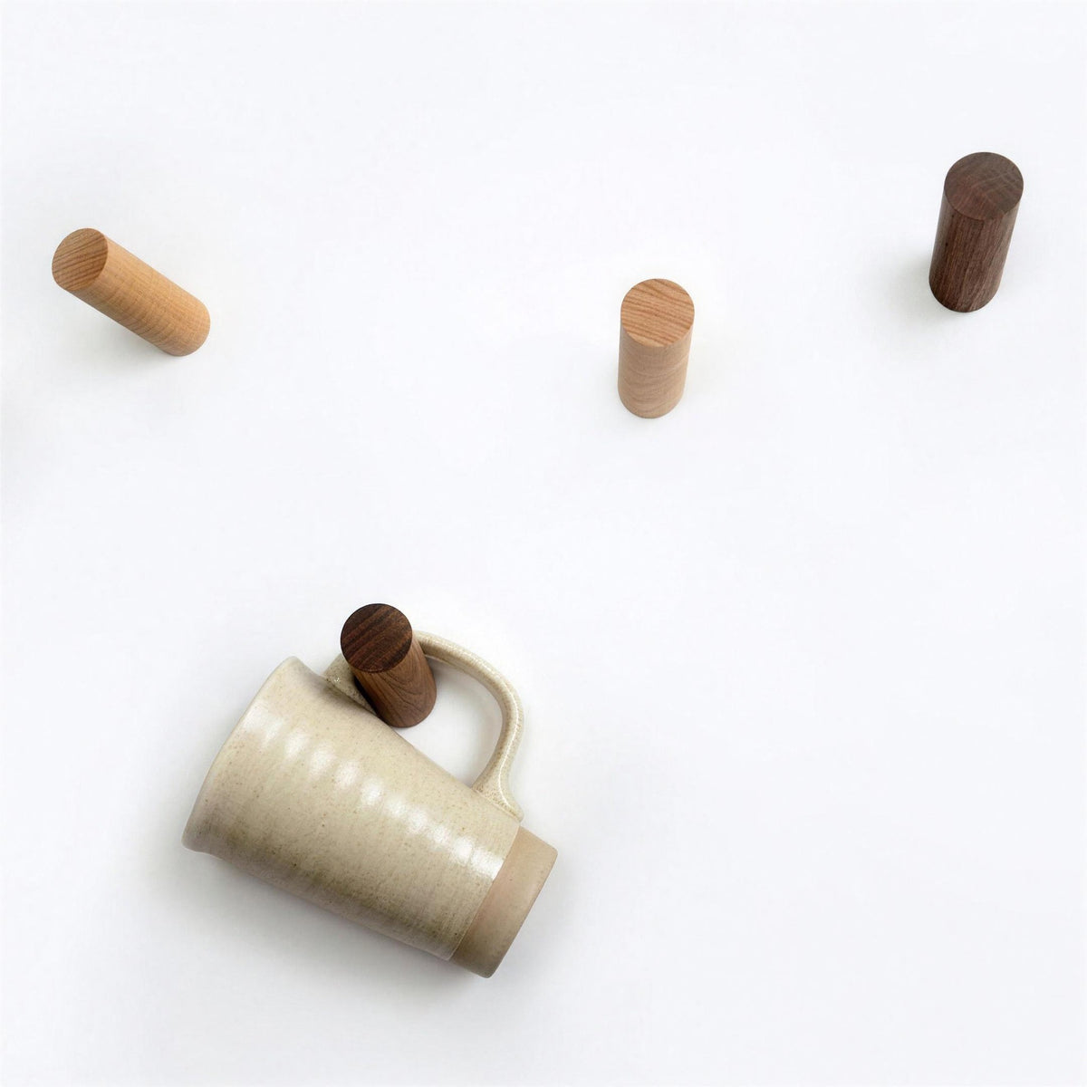 Three wood wall pegs on a wall beside a mug