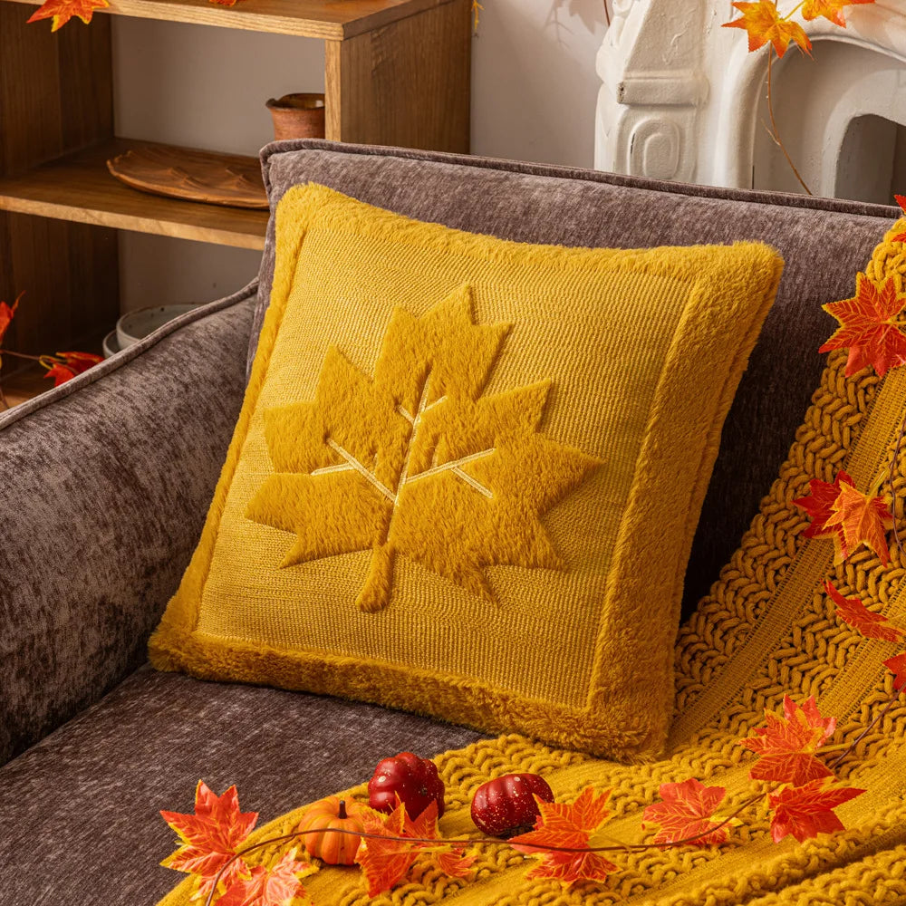 Mustard maple leaf pillow cover on a gray sofa with a mustard throw