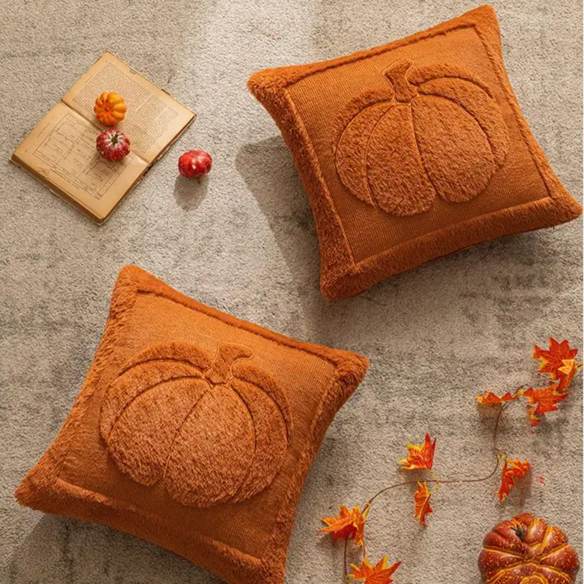 Two pumpkin pillow covers laid flat with fall leaves