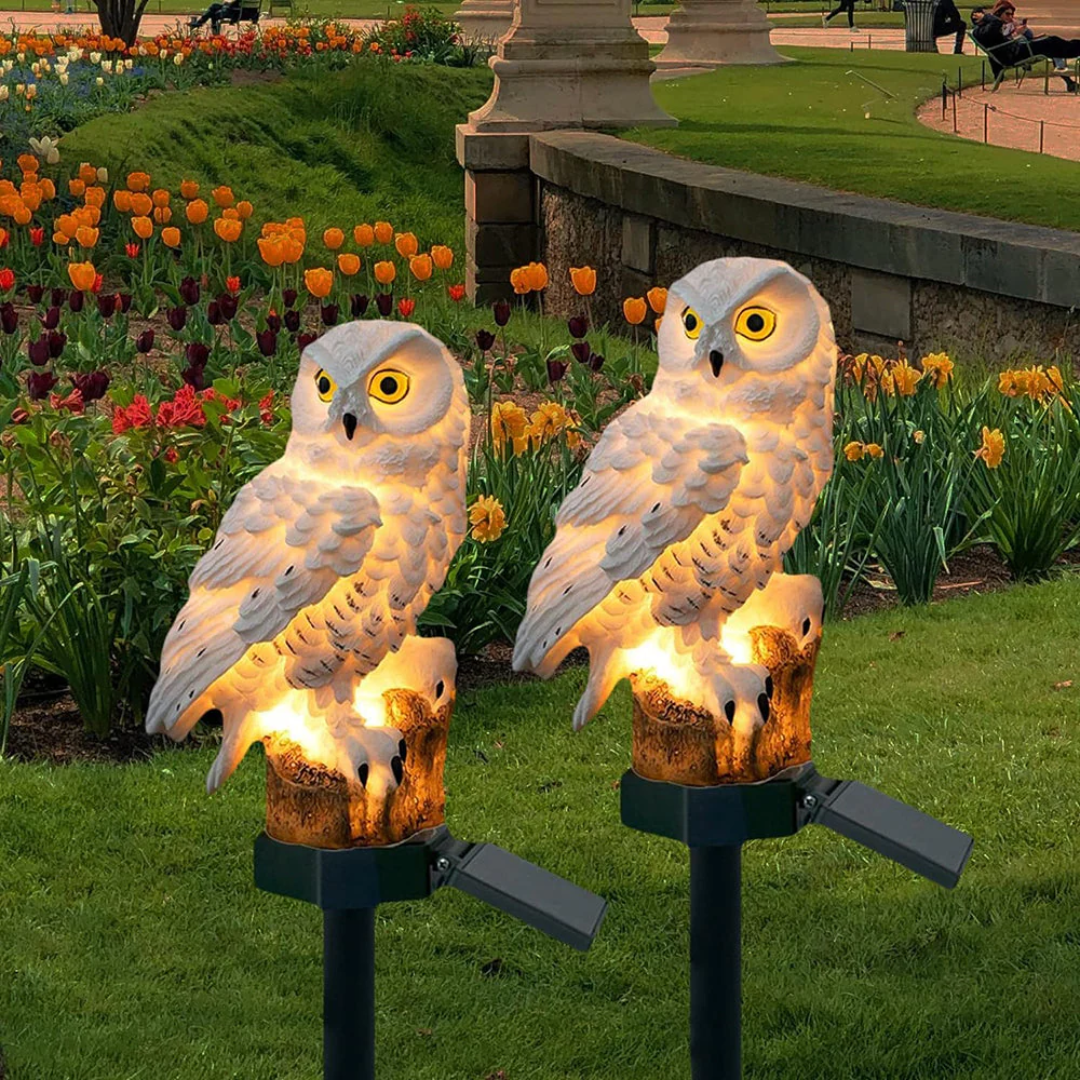 Two solar owl lights glowing among tulips at dusk
