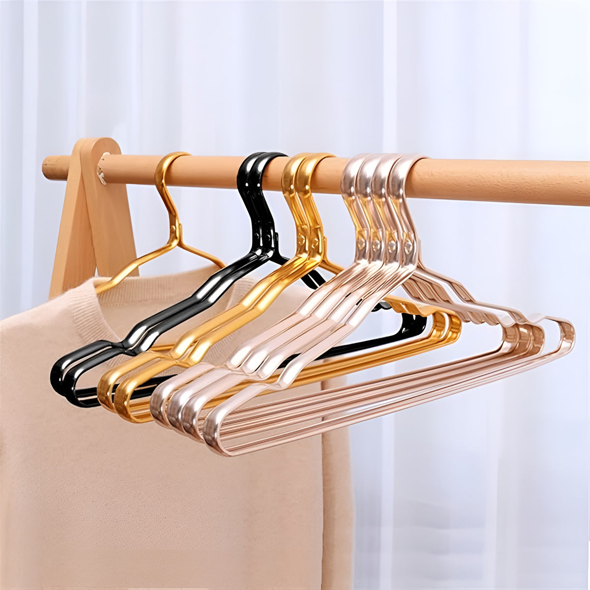 Aluminum clothes hangers in black, gold and rose pink on a wooden rack beside a sweater