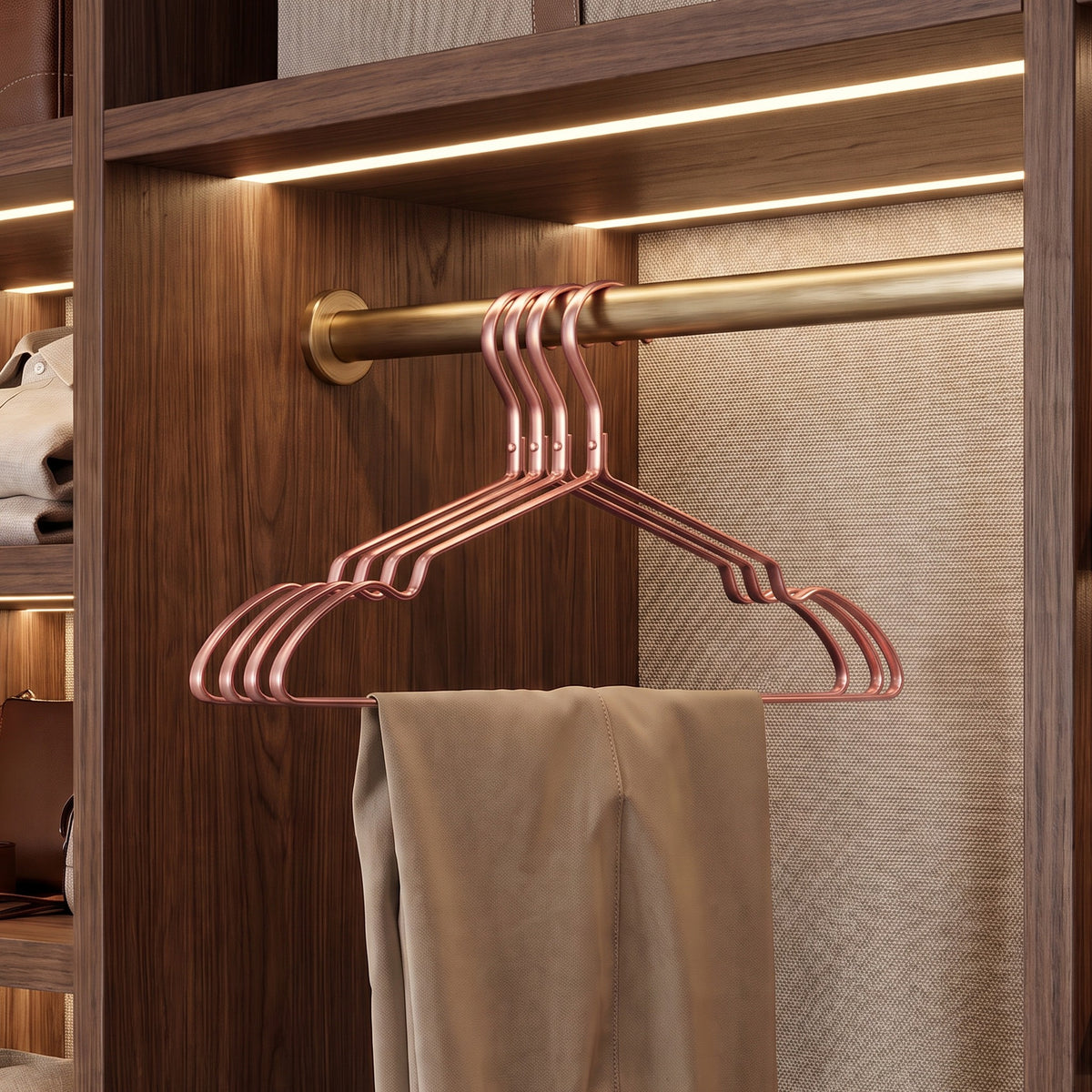 Four rose pink aluminum clothes hangers on a brass rod holding trousers in a walnut closet