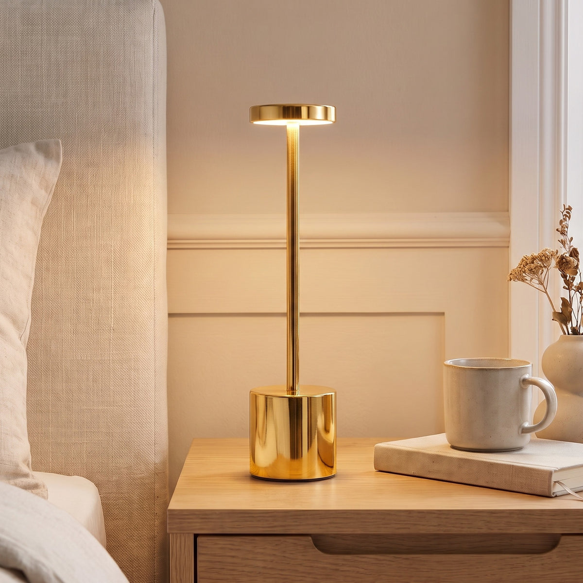 Gold Asta cordless table lamp lit on a bedside table