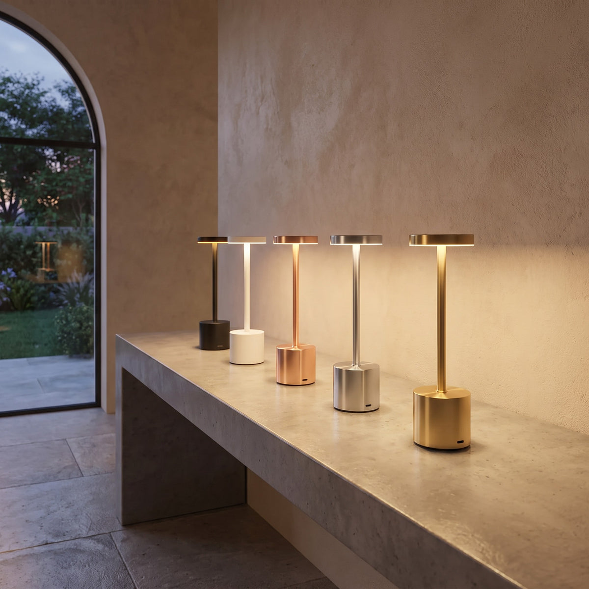 Five Asta cordless table lamps in black, white, rose, silver and gold lit on a console