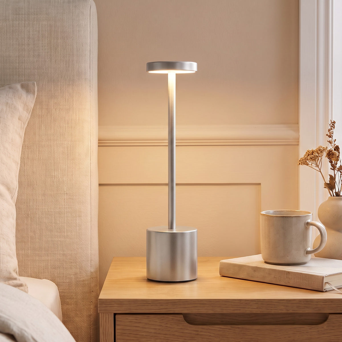 Silver Asta cordless table lamp lit on a bedside table