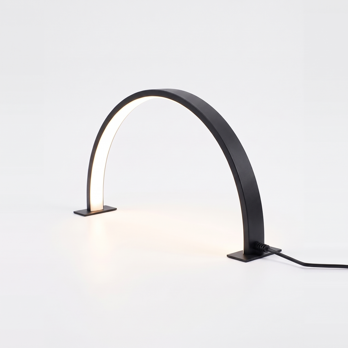 Black half moon desk lamp lit on a white background