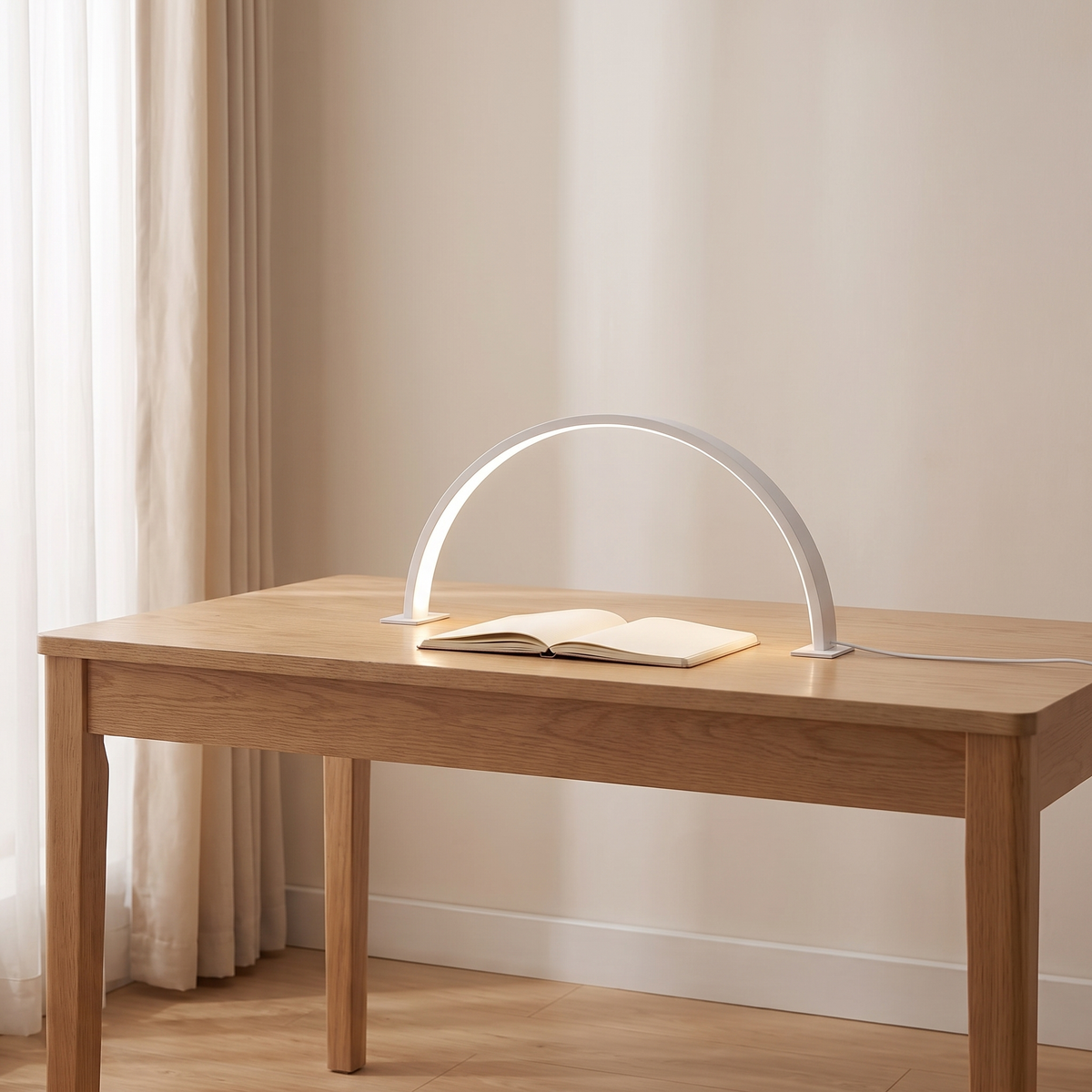 Bryn half moon desk lamp in white lit over an open notebook on a light oak desk