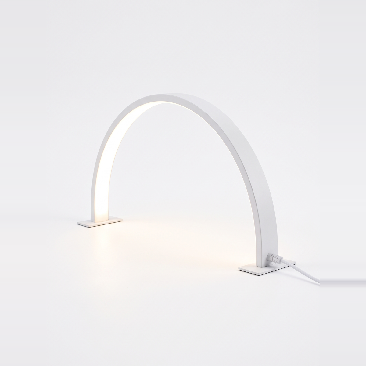 White half moon desk lamp lit on a white background