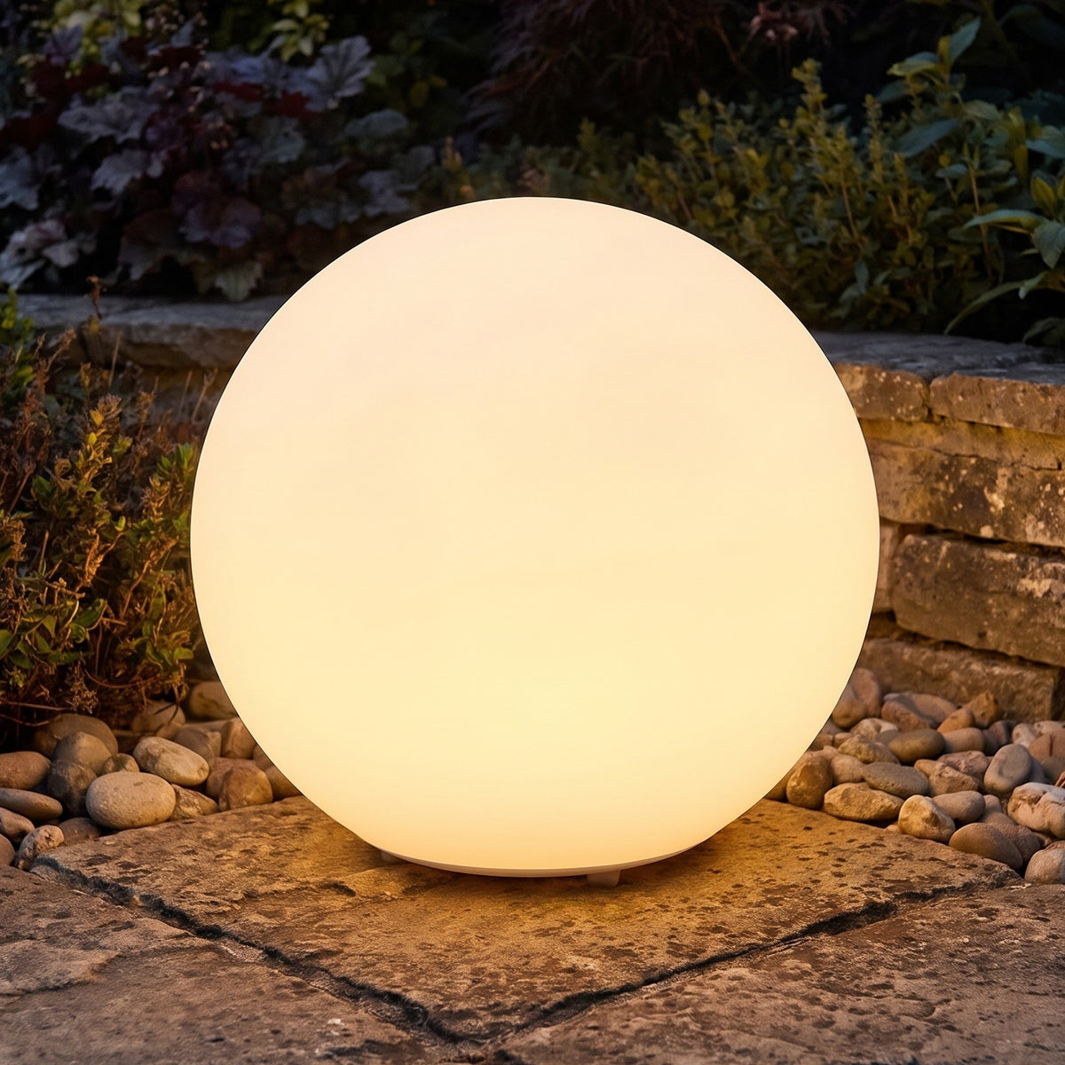 Ellen globe garden light glowing on a stone patio beside pebbles