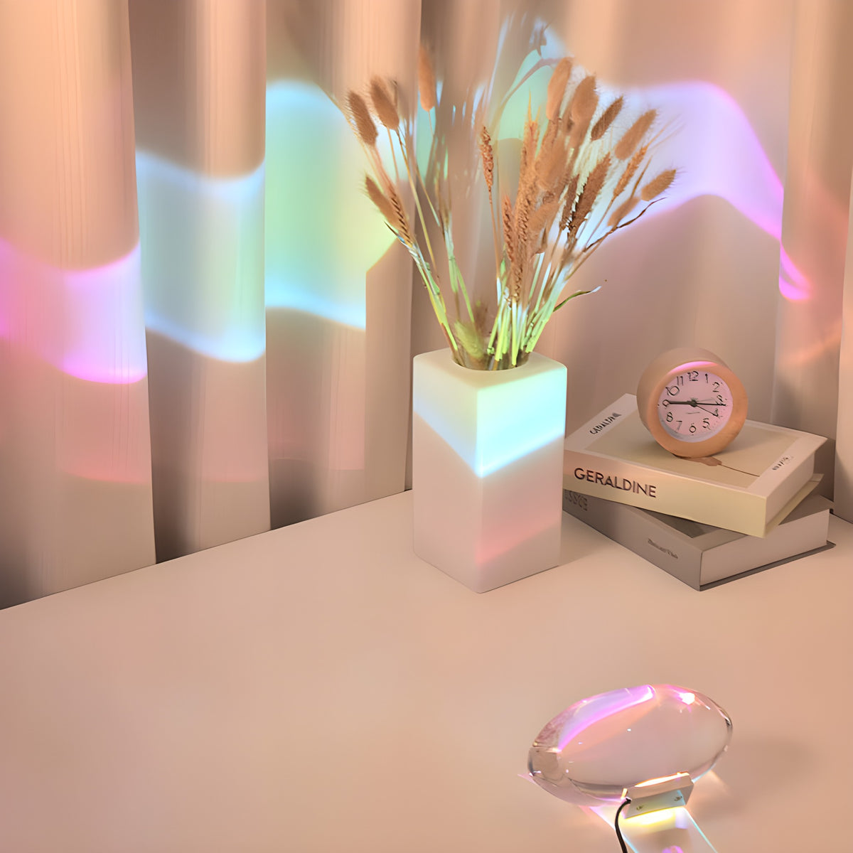 Elna projection lamp beside a vase of dried grass and books, color across the curtains