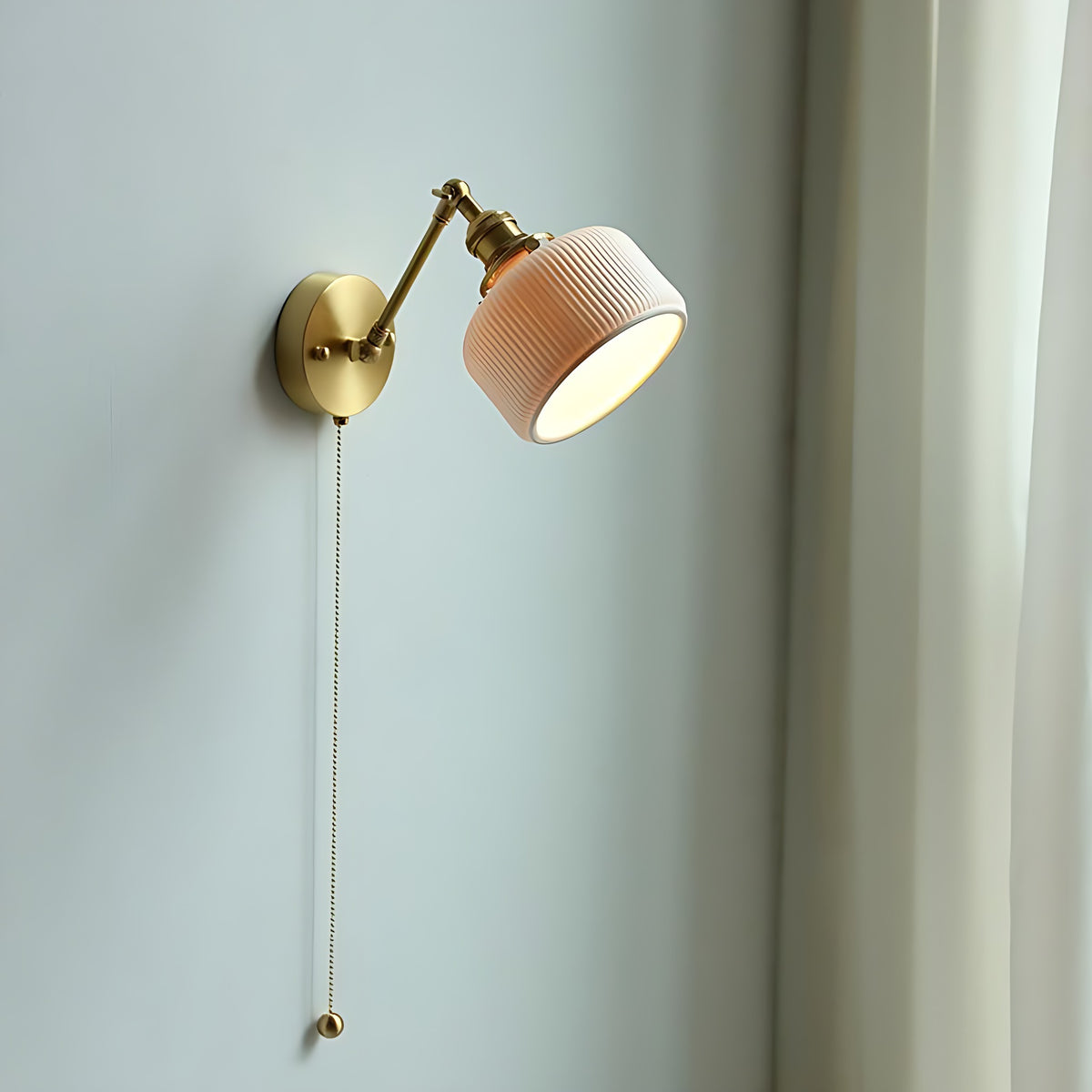 Swing arm wall sconce with the shade tilted, on a pale wall beside a curtain