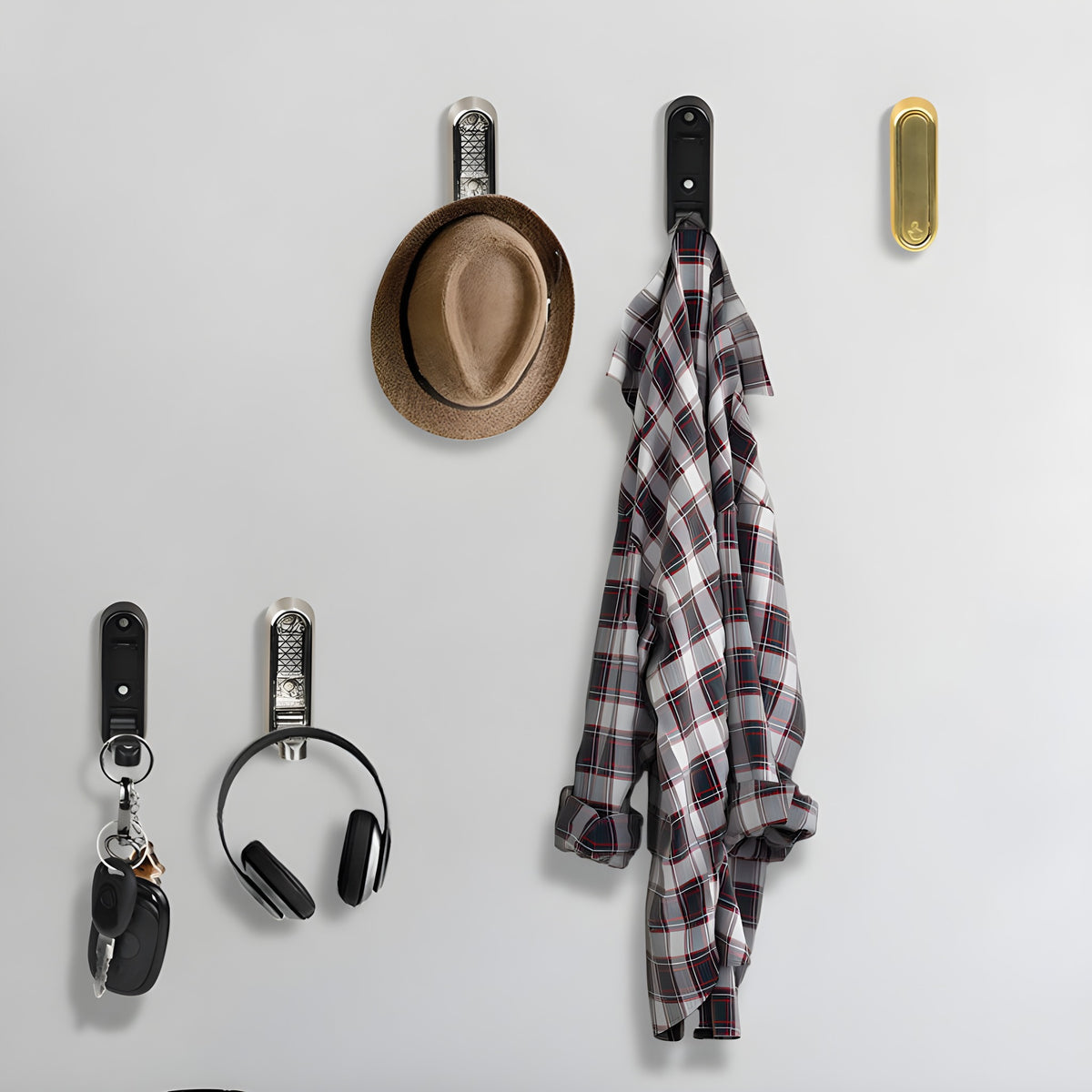 A row of folding wall hooks holding keys, headphones, a hat and a shirt