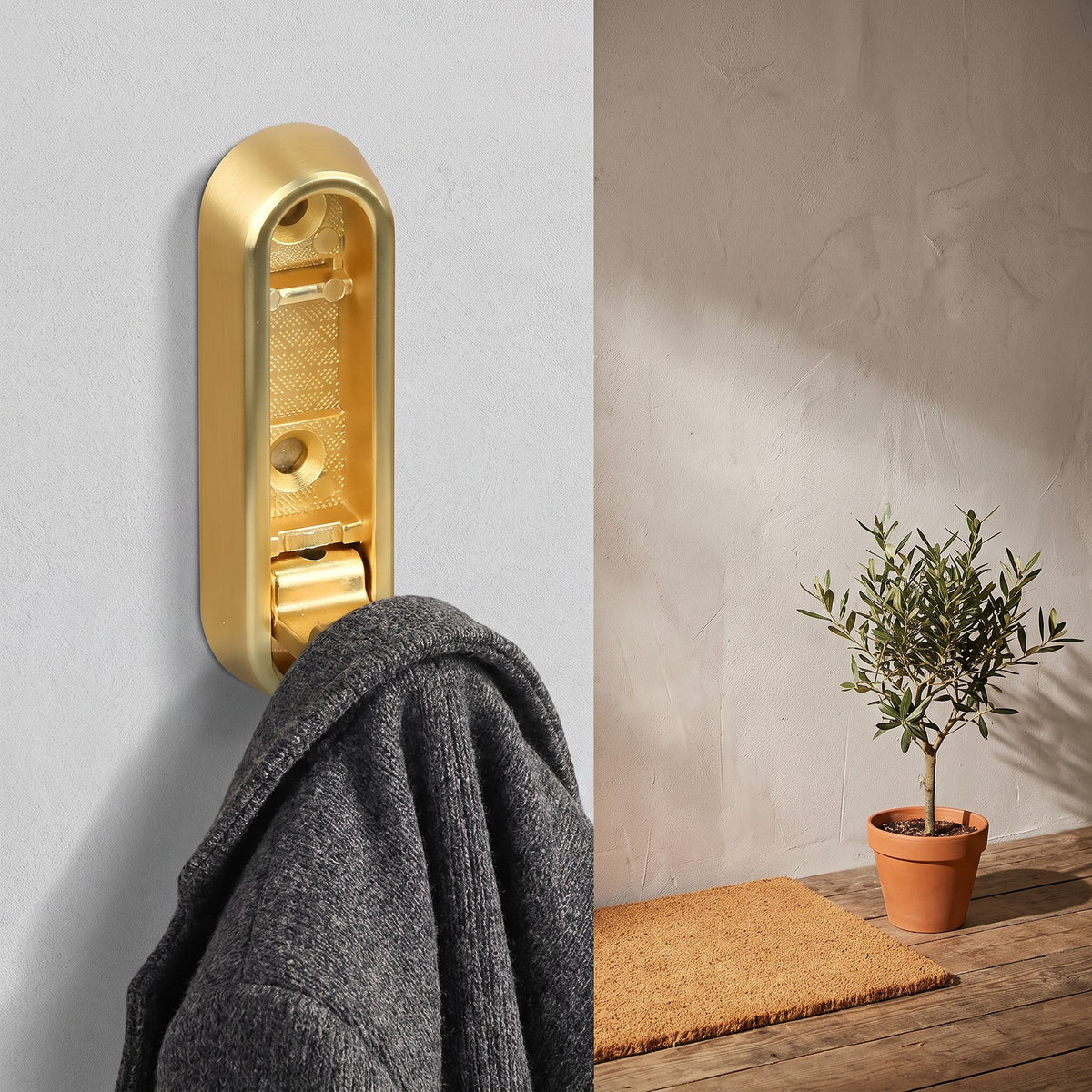 Gold folding wall hook holding a wool coat on an entryway wall