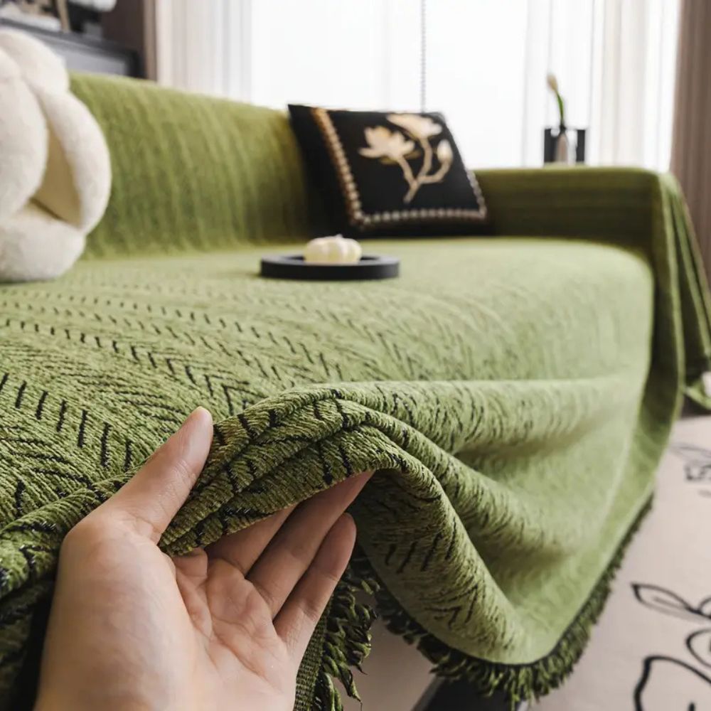 Hand lifting the tasseled edge of the green chenille sofa cover to show its weight