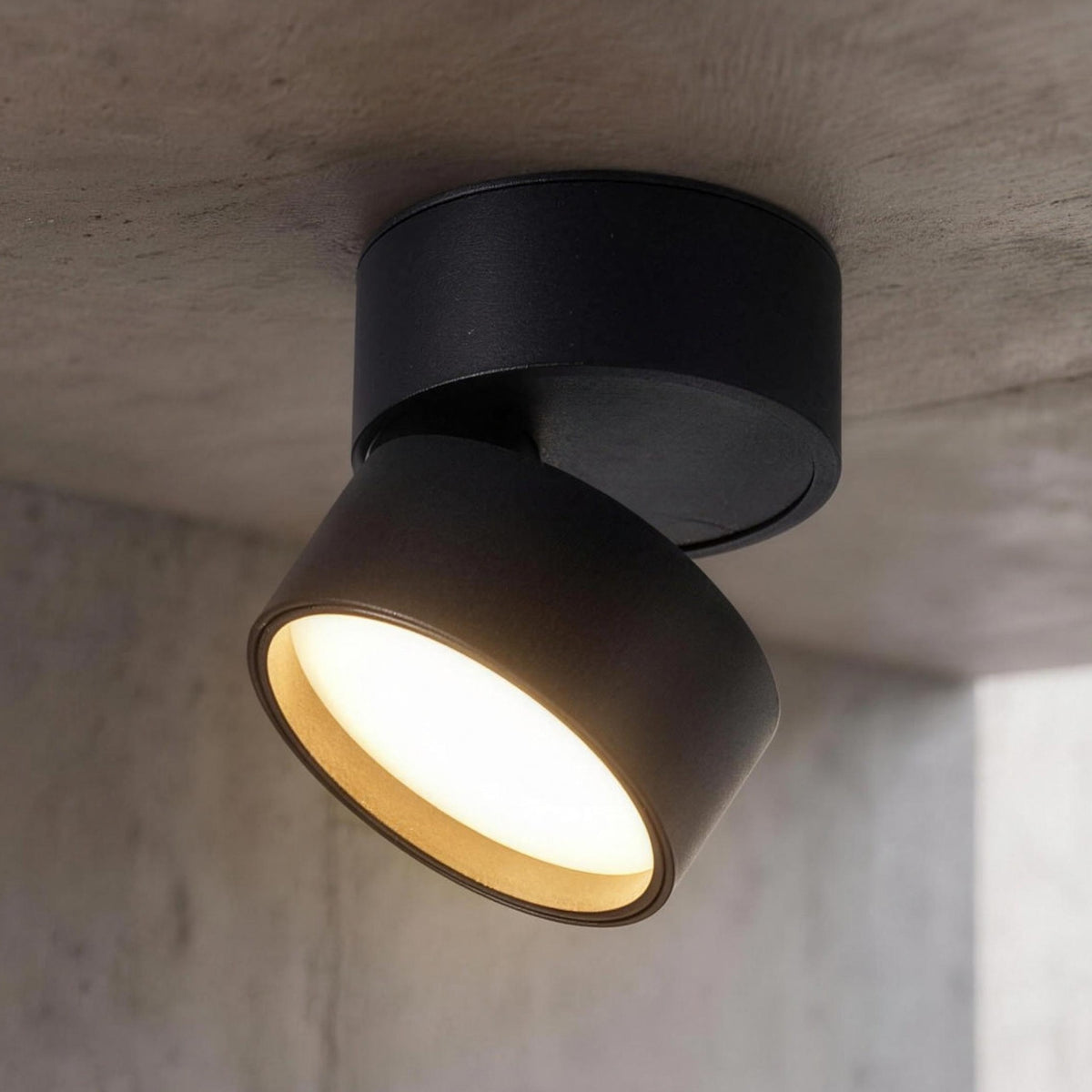 Ilse LED ceiling spotlight, black, head tilted and lit on a concrete ceiling