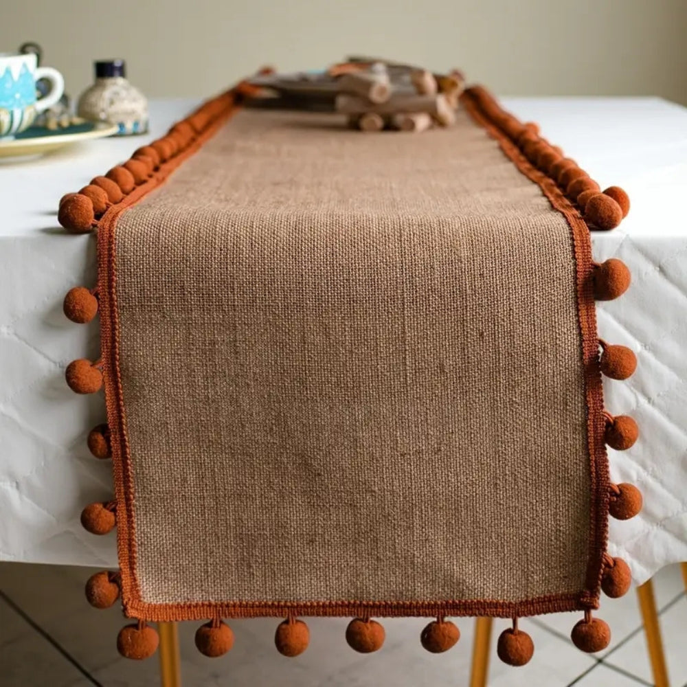 Jute table runner with pom pom trim over a white tablecloth