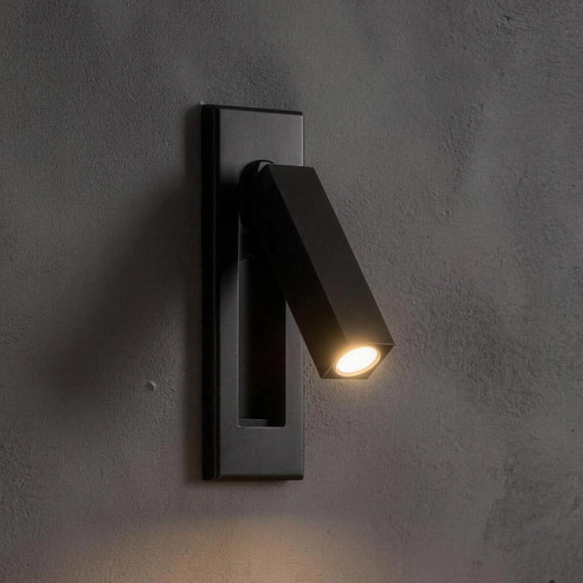 Kaia LED reading wall light, square, matte black, recessed in a gray plaster wall above a walnut nightstand