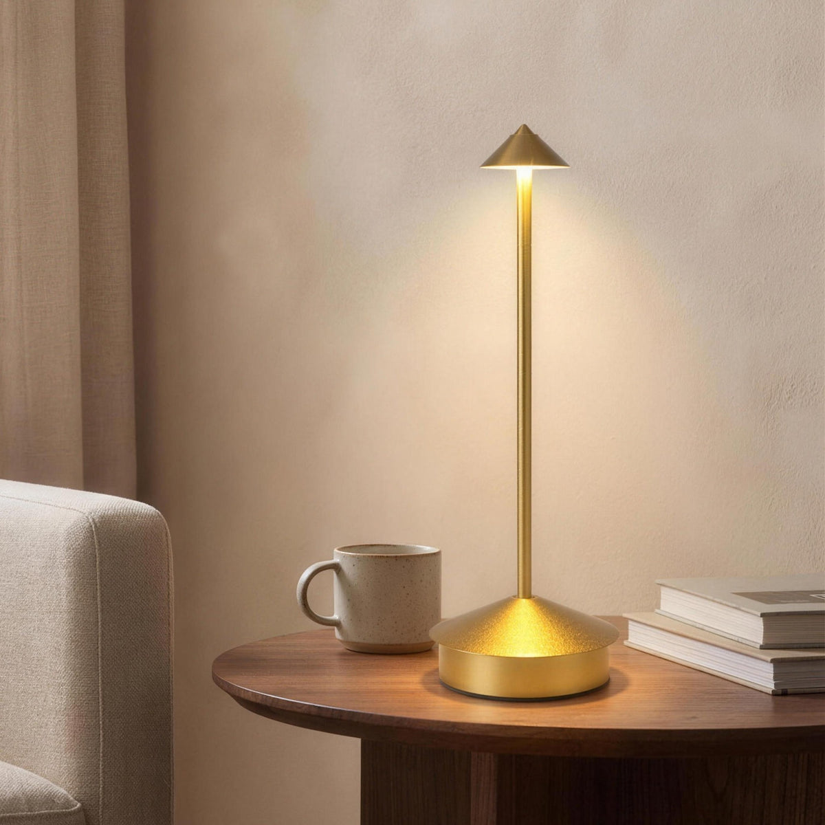 Gold Lene cordless table lamp lit on a walnut side table by an armchair