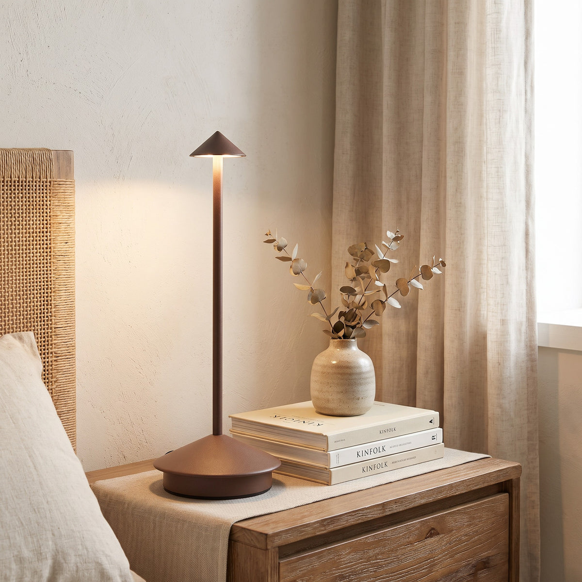 Brown Lene cordless table lamp lit on a nightstand beside books