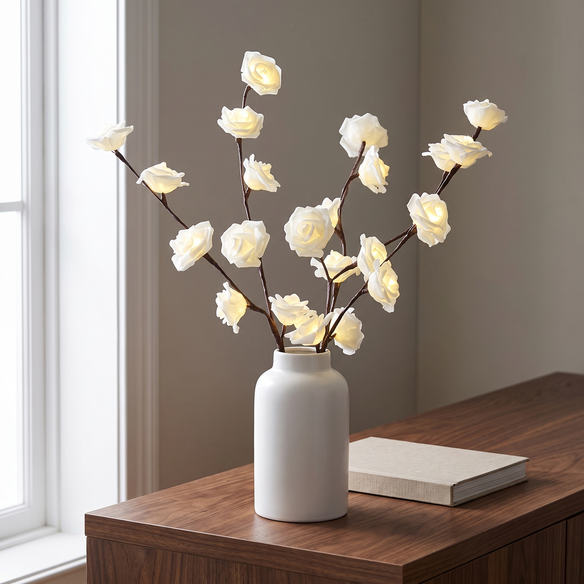 Lighted branches with white roses in a white vase on a walnut console