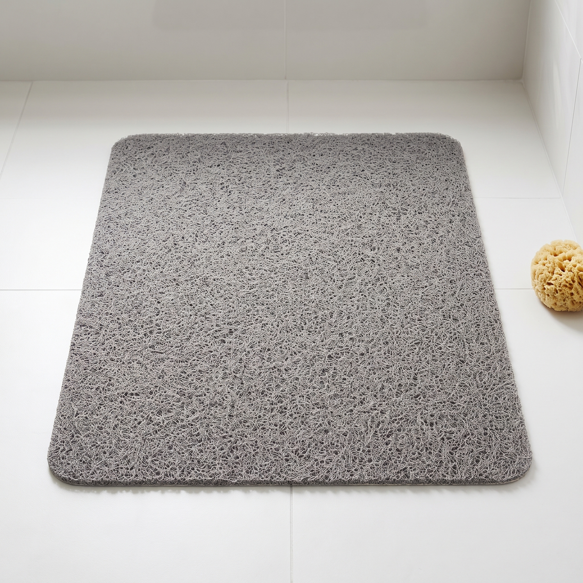 Gray loofah weave shower mat on a white tile floor