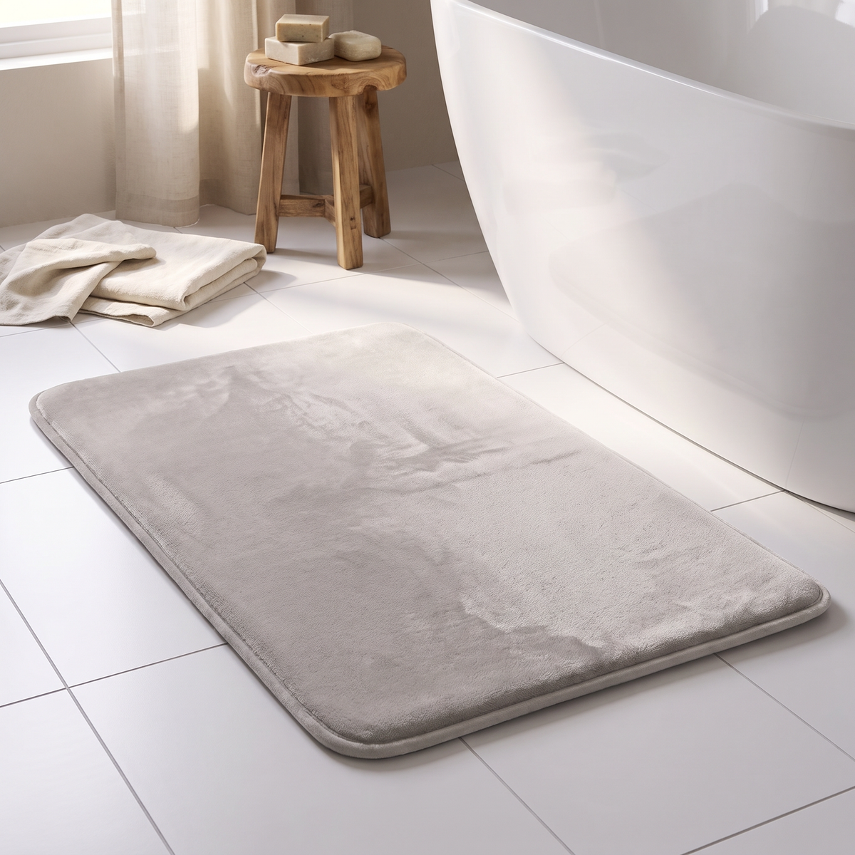 Close view of a light gray velvet bath mat beside a tub