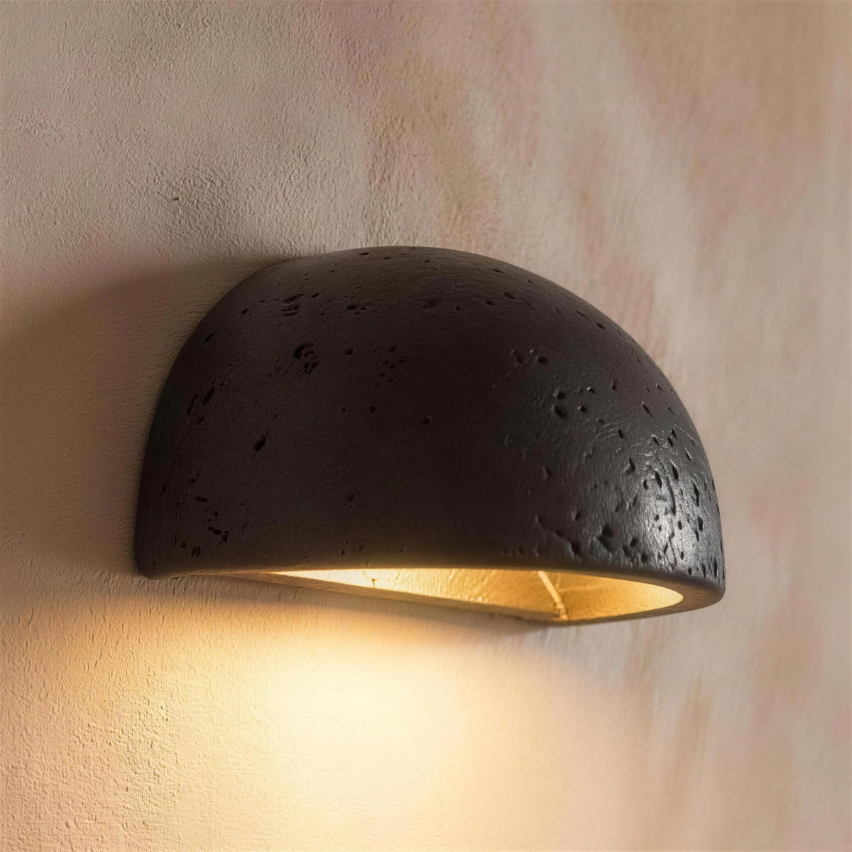 Mira LED wall sconce, black travertine half dome, lit