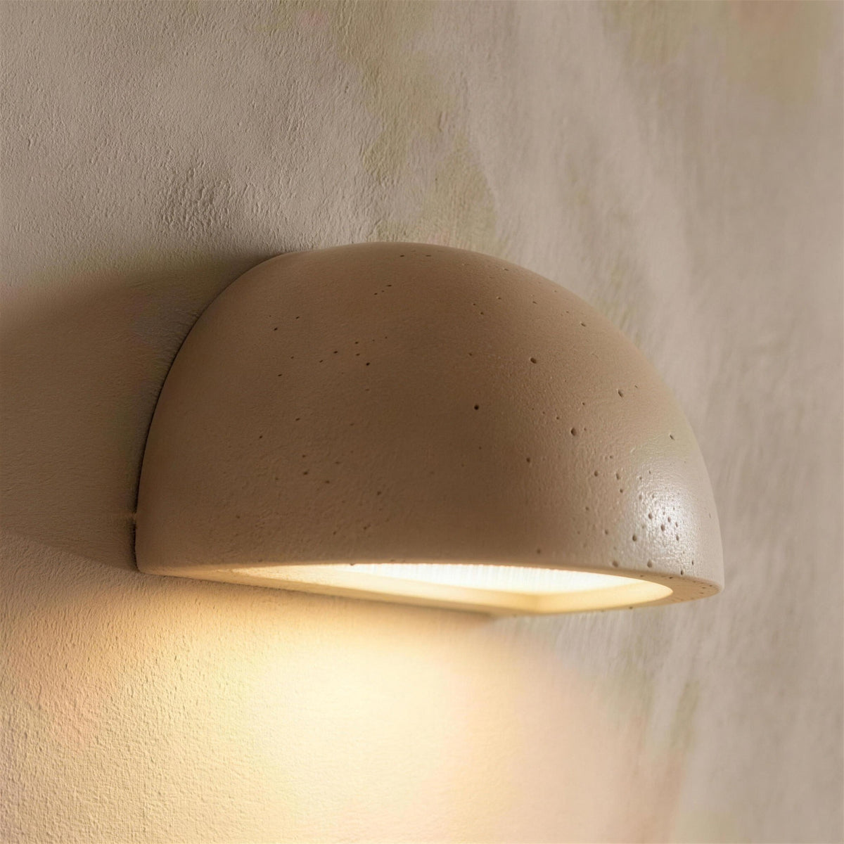 Mira LED wall sconce, light yellow travertine half dome, lit