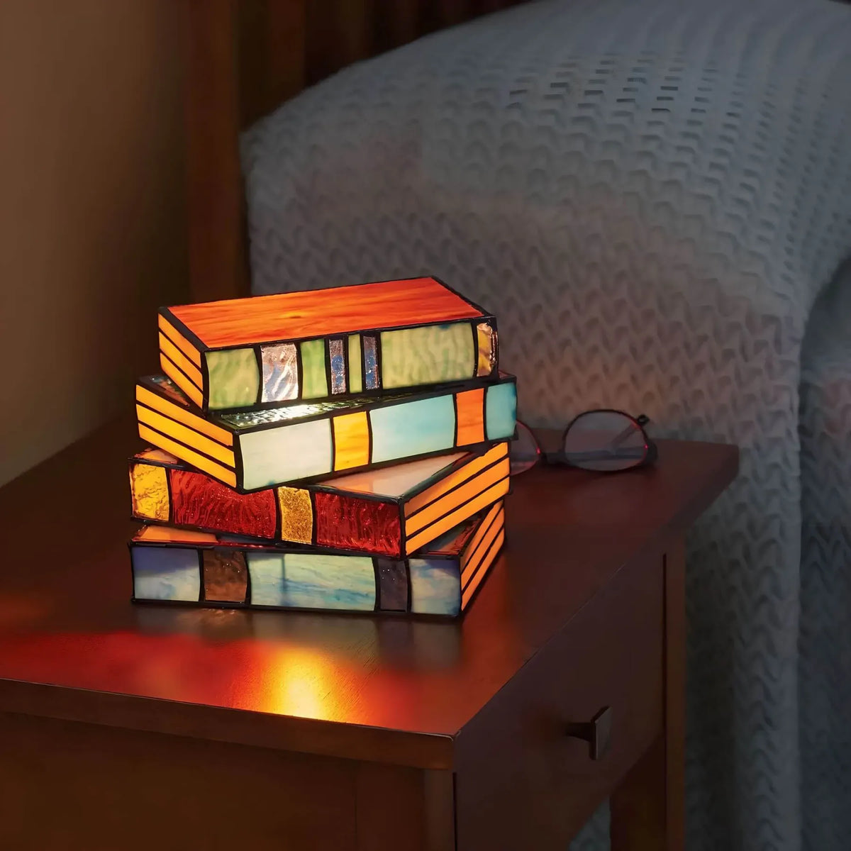 Stained glass book stack lamp lit on a wood side table at night
