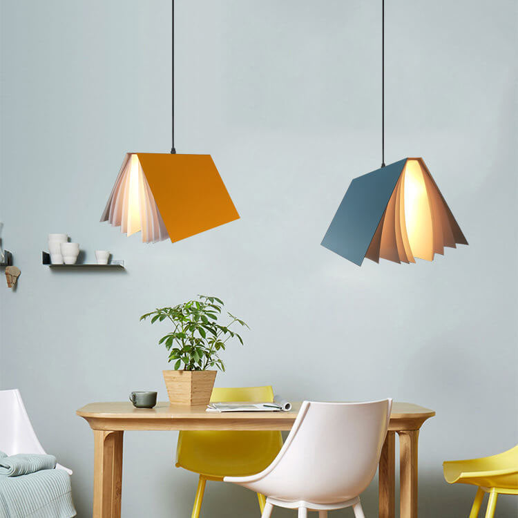 Yellow and blue book pendants hanging over a wooden dining table with yellow chairs