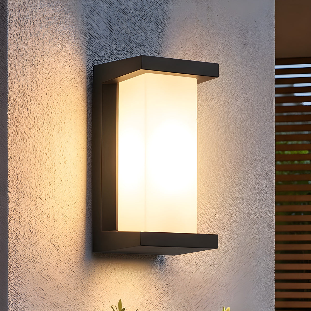 Outdoor motion sensor wall light lit on a rendered wall beside a planter