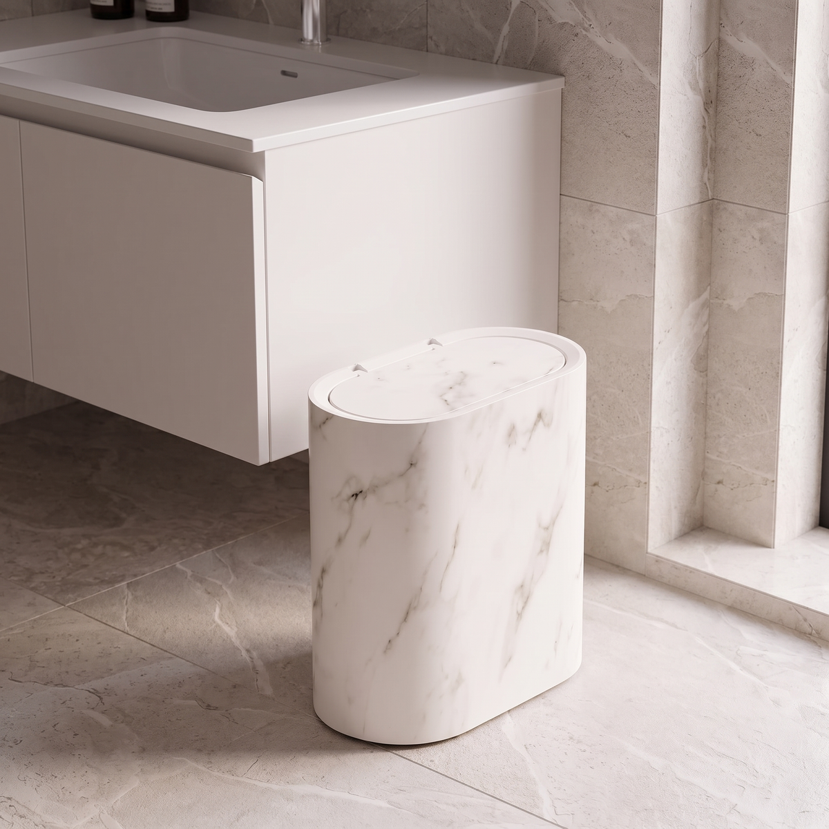 Cream white marble oval waste bin with flip lid on a stone bathroom floor beside a vanity