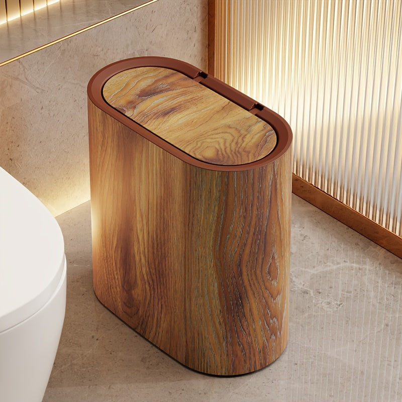 Oval waste bin in light wood grain beside a toilet in a warm lit bathroom