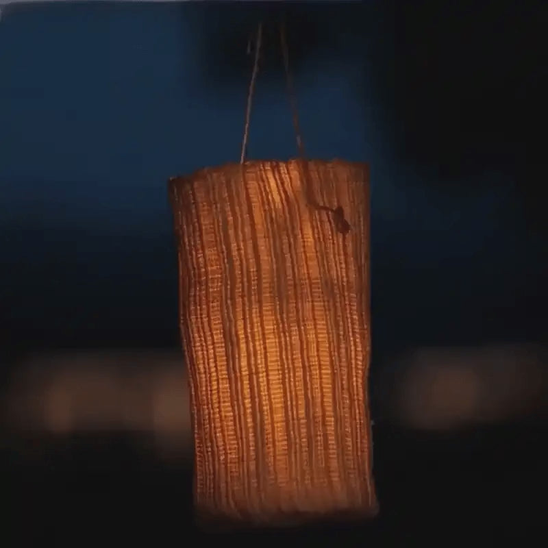 Vejle woven lantern glowing as it sways on its cord at dusk