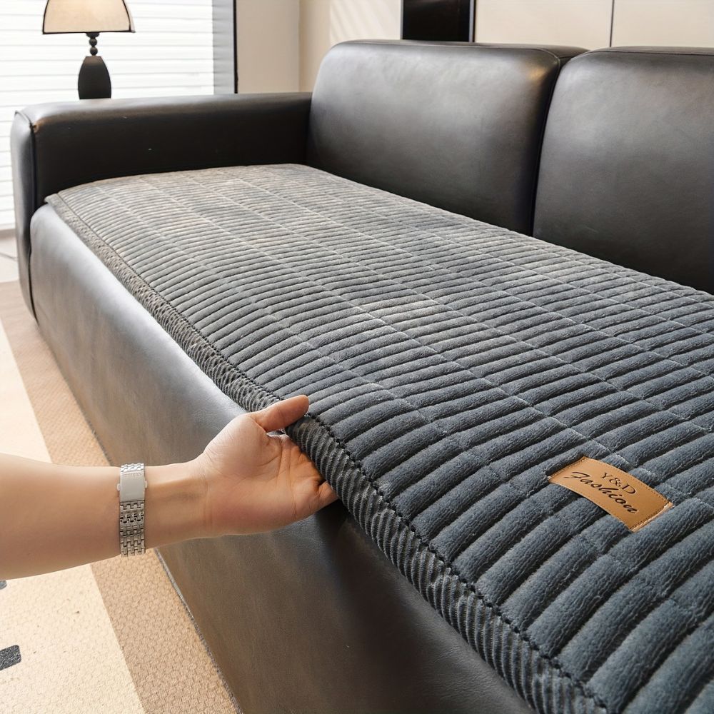 Hand lifting the edge of a slate gray quilted couch cover to show its thickness