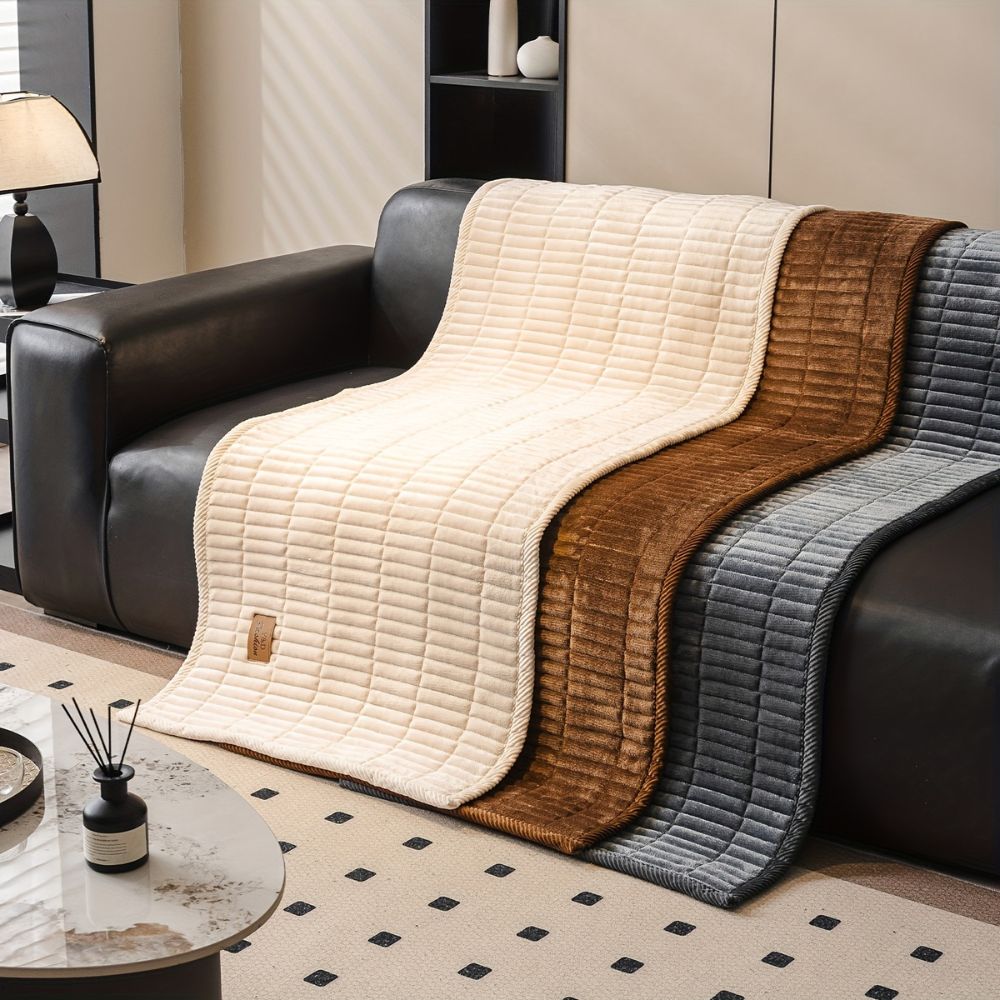 Quilted couch covers in cream, amber and slate gray laid side by side on a sofa