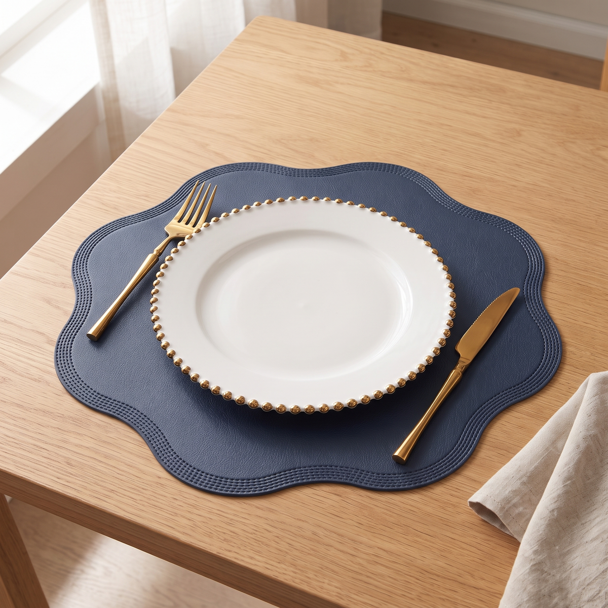 Scalloped placemat in black with a white plate and gold cutlery on an oak table