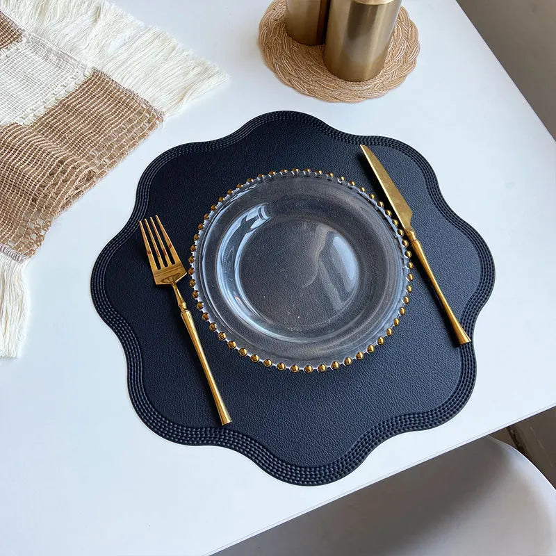 Black scalloped placemat with a glass plate and gold cutlery from above