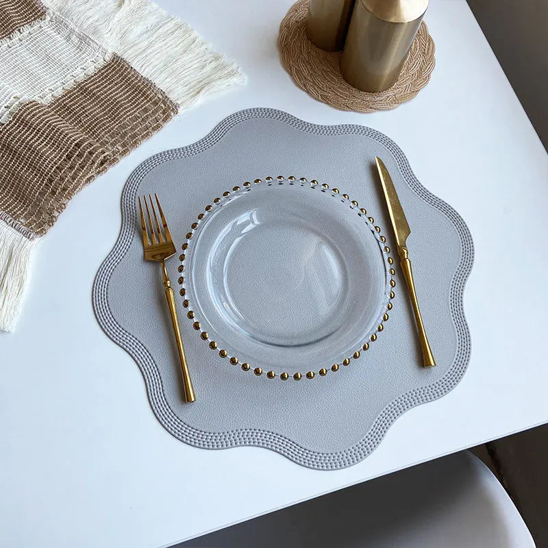 Gray scalloped placemat with a glass plate and gold cutlery from above