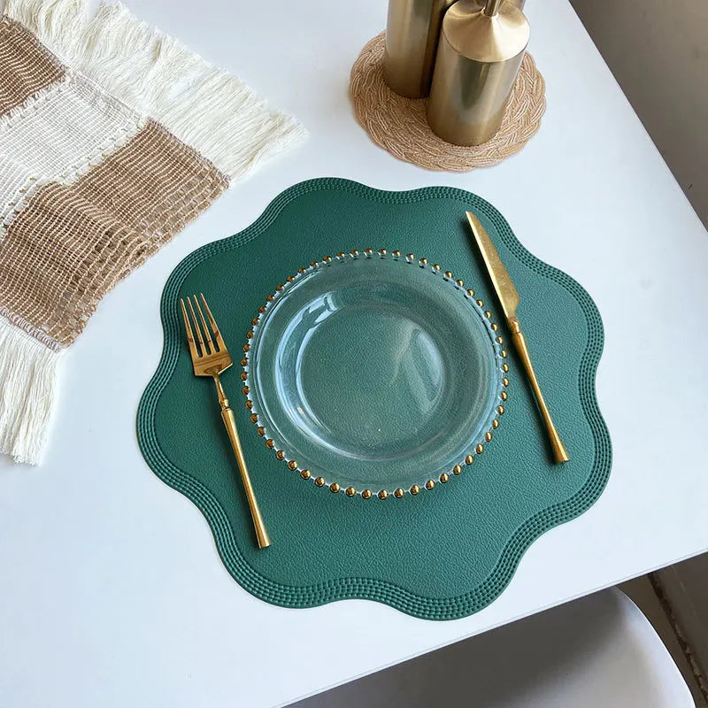 Green scalloped placemat with a glass plate and gold cutlery from above