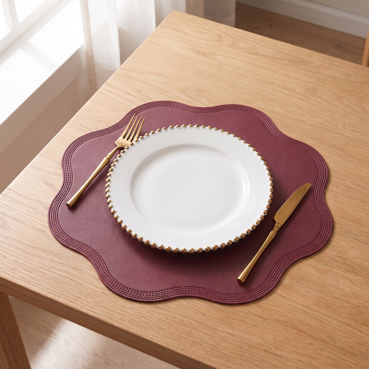 Scalloped placemat in red with a white plate and gold cutlery on an oak table