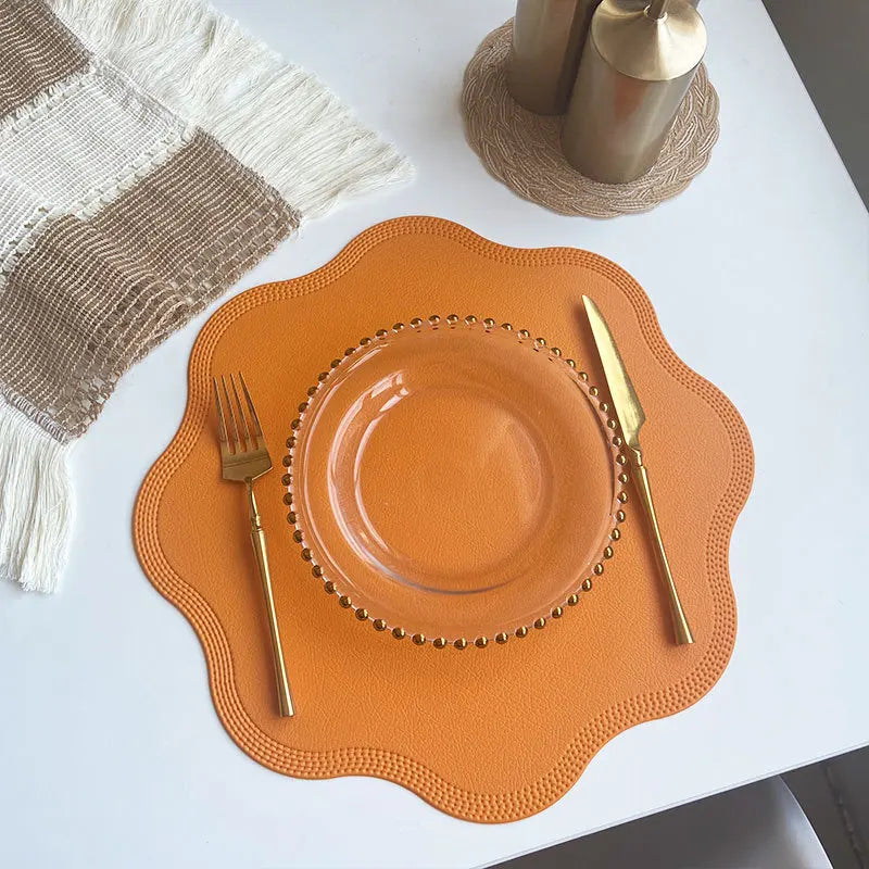 Yellow scalloped placemat with a glass plate and gold cutlery from above