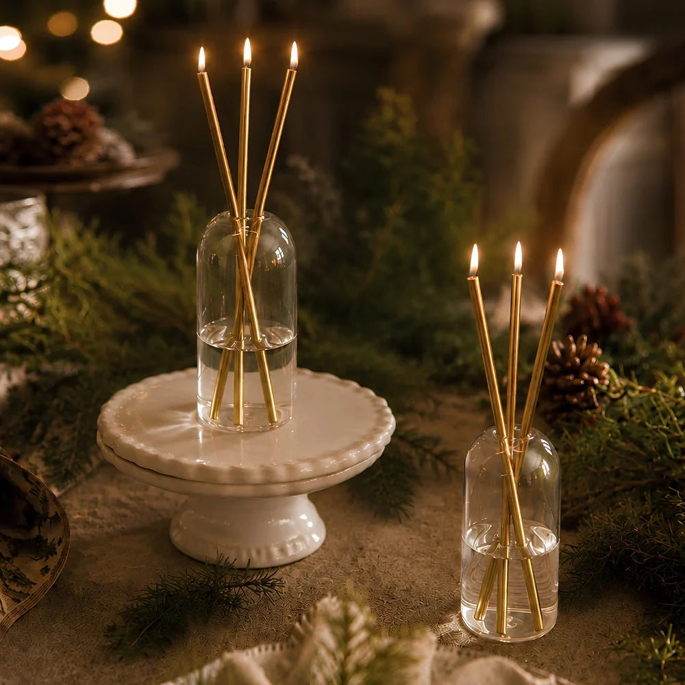 Two sets of Skive gold oil candles among evergreen sprigs