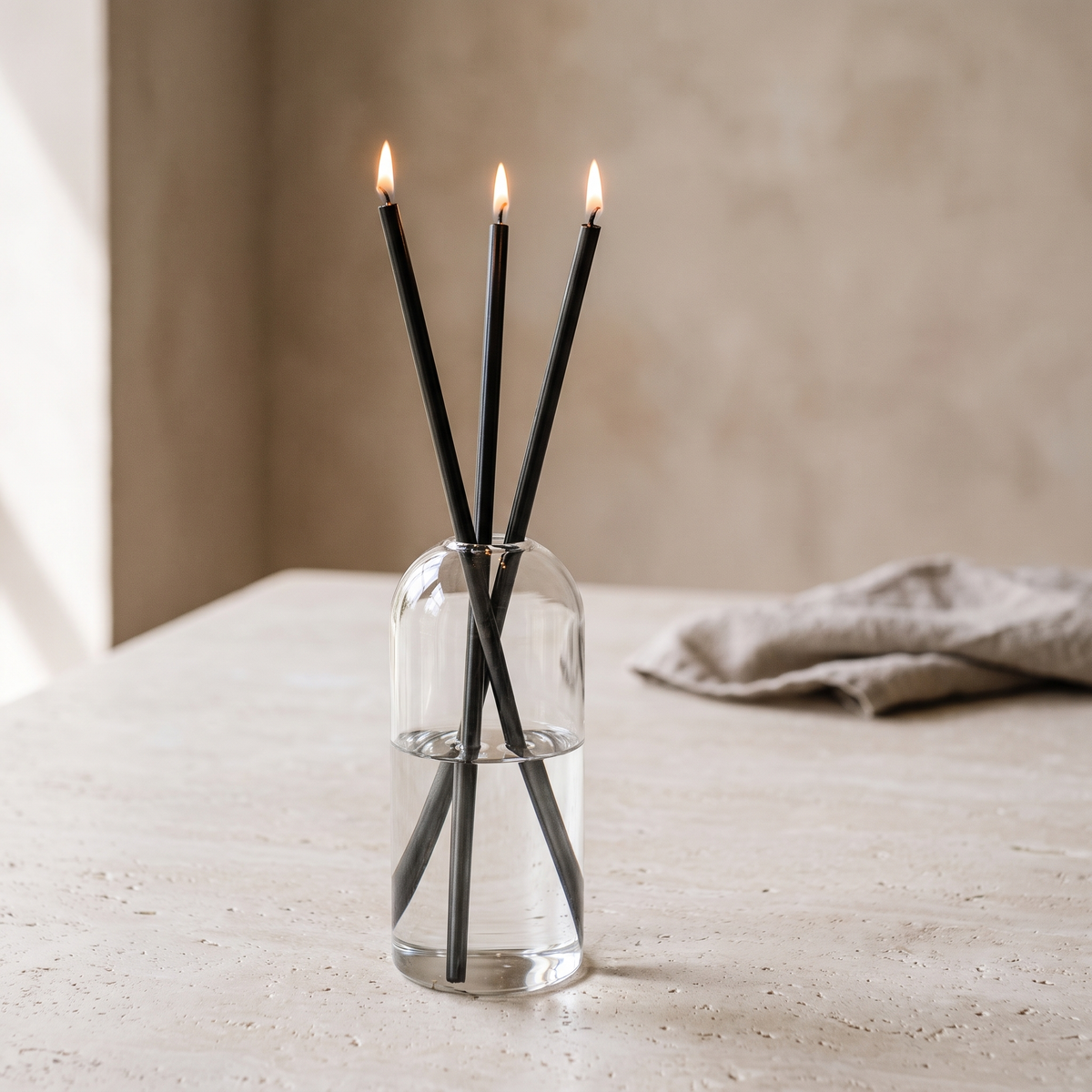 Skive oil candles with black stems lit on a limestone table