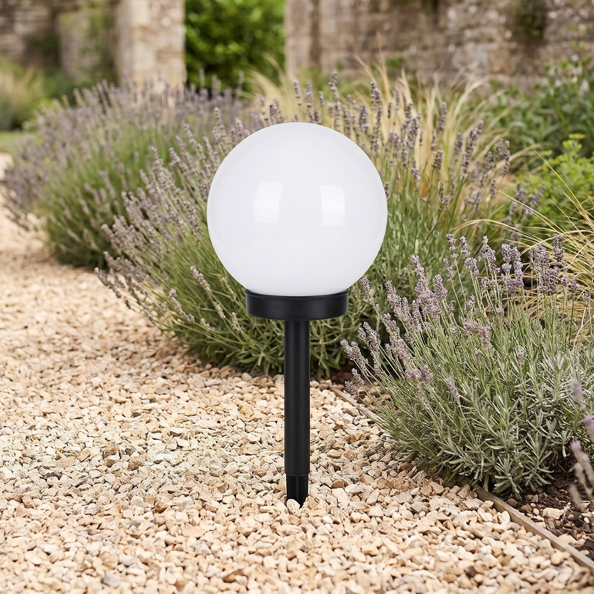 Solar globe stake light with a cool white globe in a gravel bed beside lavender